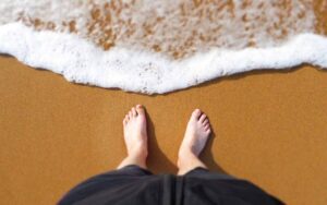 pieds d'une personne sur la plage près d'une vague